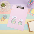A pink clipboard with a cute cartoon dinosaur illustration and speech bubbles reading 'I like you' and 'Me too', styled on a pink background with a lace doily and a lined notebook.