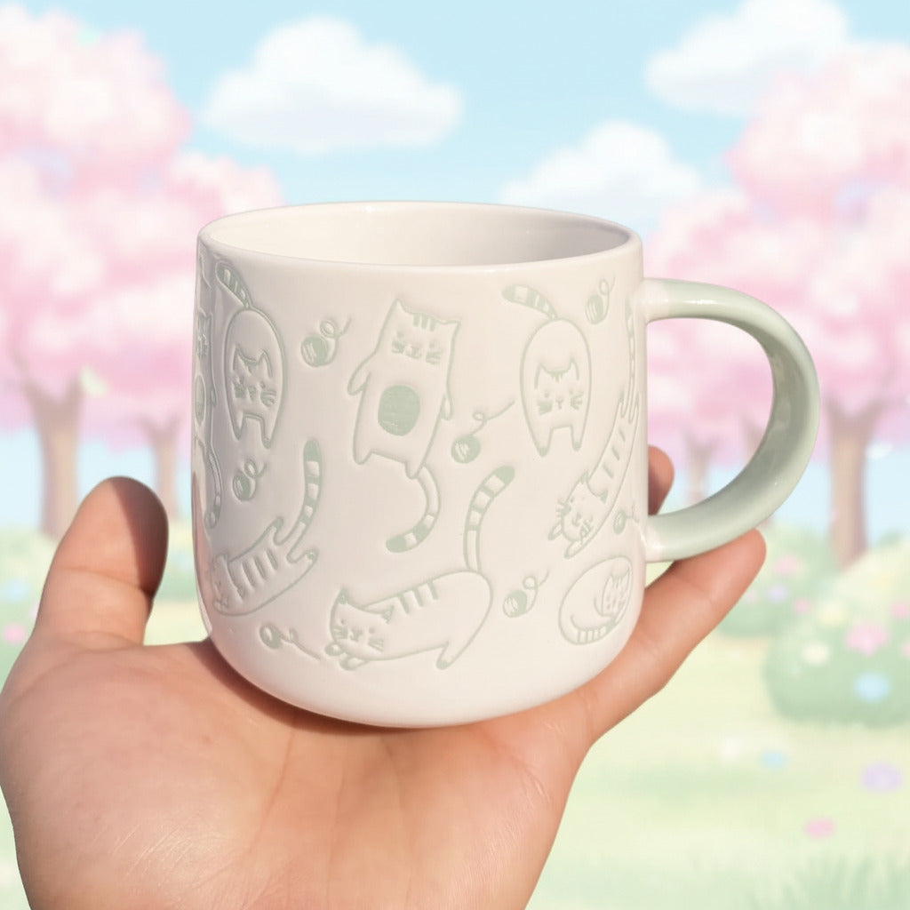 White mug with green cat designs held in a hand outdoors