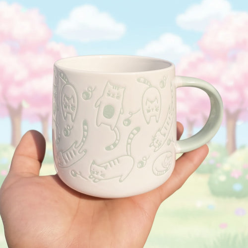 White mug with green cat designs held in a hand outdoors