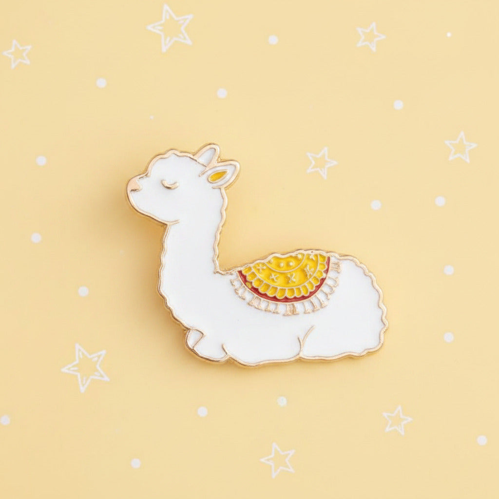 A small alpaca-shaped enamel pin with a white body, gold outline, and a yellow patterned saddle on its back, shown on a plain white and pastel yellow background.