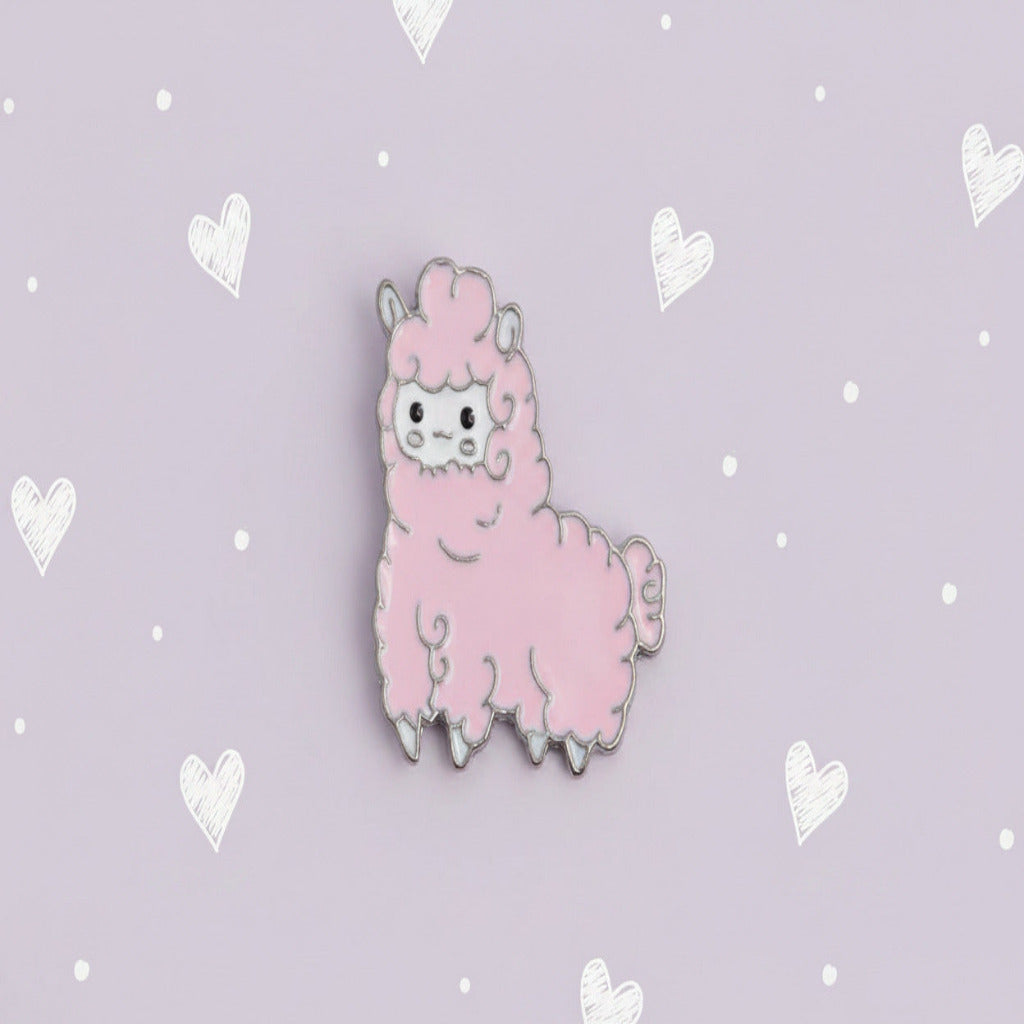 A pink alpaca enamel pin with a silver metal border, featuring a cute cartoon face and fluffy textured body, shown on a plain white background.