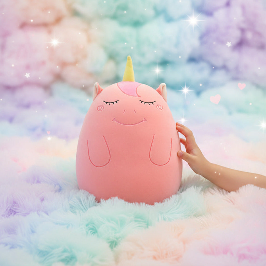 Pink plush toy with a yellow horn on a bed