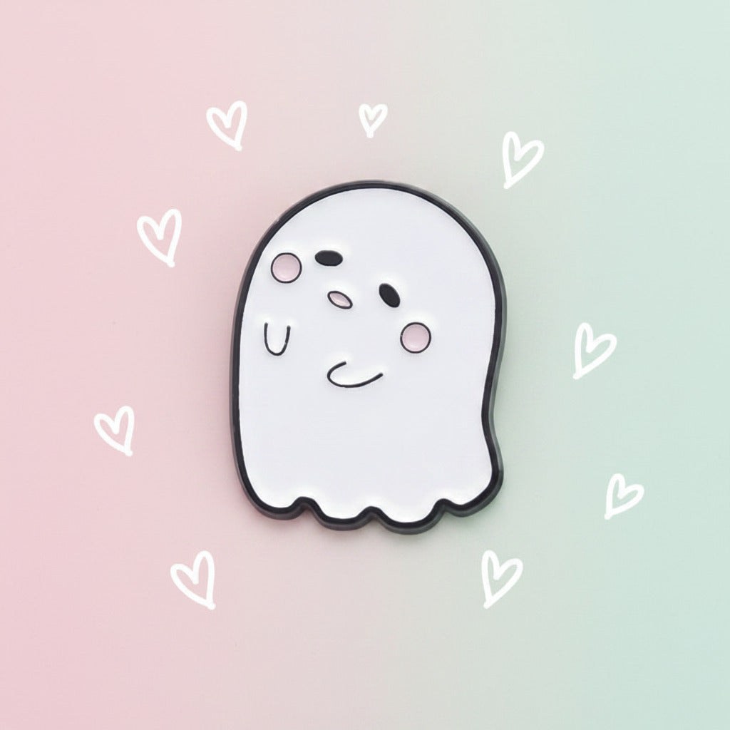 A cute cartoon ghost charm or pin with a white face, black outline, and pink cheeks on a pastel colored background.