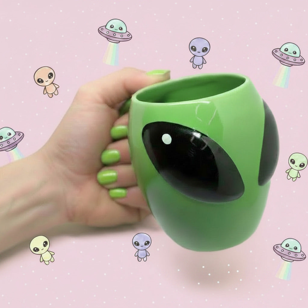 Green alien-shaped cup held by a hand on a pink background