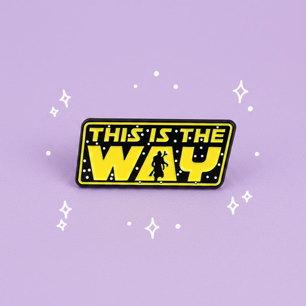 A rectangular yellow and black pin with the text 'THIS IS THE WAY' in a Star Wars style, featuring a small silhouette of a droid walking down the center, shown on a plain white background.