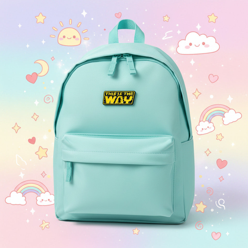 A rectangular enamel pin with the text 'THIS IS THE WAY' in yellow over a black starry background, photographed on a white surface with a light cyan background and kawaii environment.