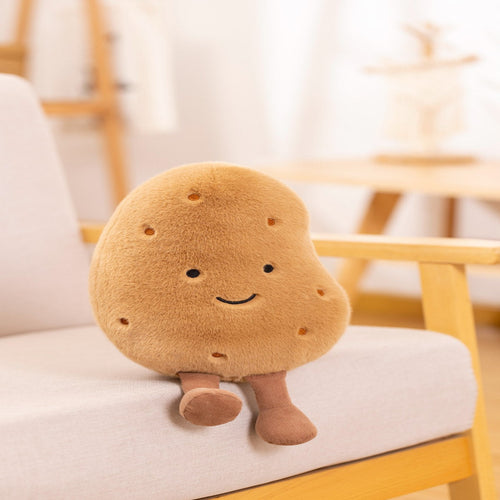 A cute potato-shaped plush toy with a smiling face and small legs, sitting on a light-colored armchair in a softly blurred indoor setting.