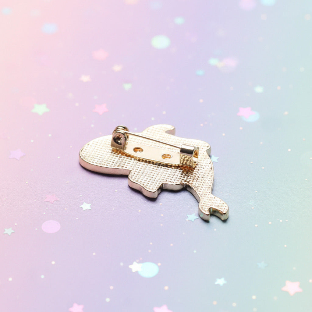 A gold-colored dinosaur-shaped safety pin brooch with a textured pattern, shown on a soft, out-of-focus light blue and white background.
