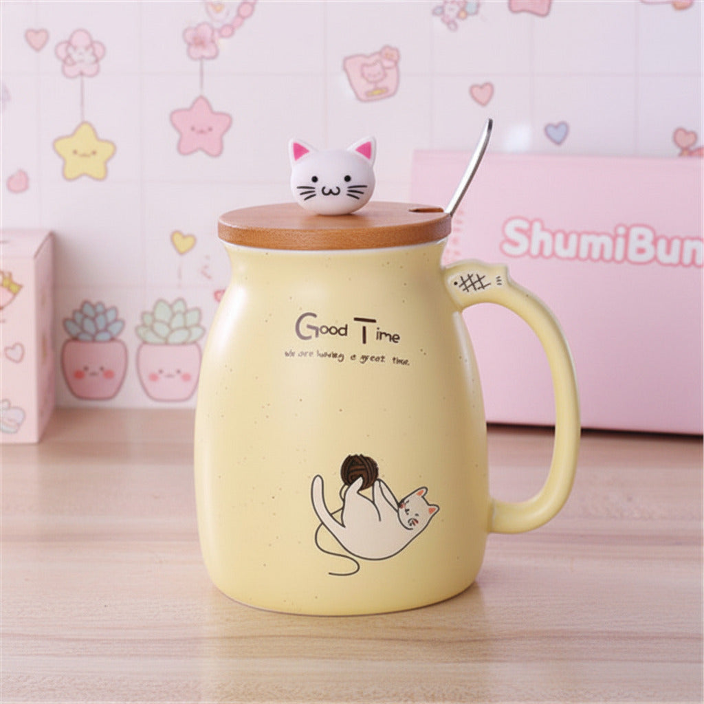 A pale yellow ceramic mug with a wooden lid and a small white cat figurine on top, set on a wooden table with a spoon resting inside. The mug features the text 'Good Time' and a cute cat illustration.