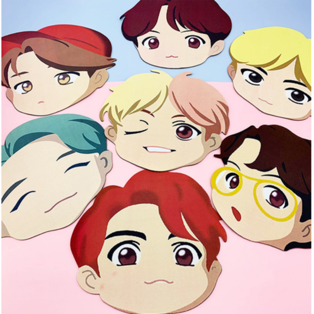 A set of cartoon-style character head cutouts or stickers arranged on a pink and light blue background. The characters have different hair colors including red, yellow, brown, teal, and black, with one wearing yellow glasses.
