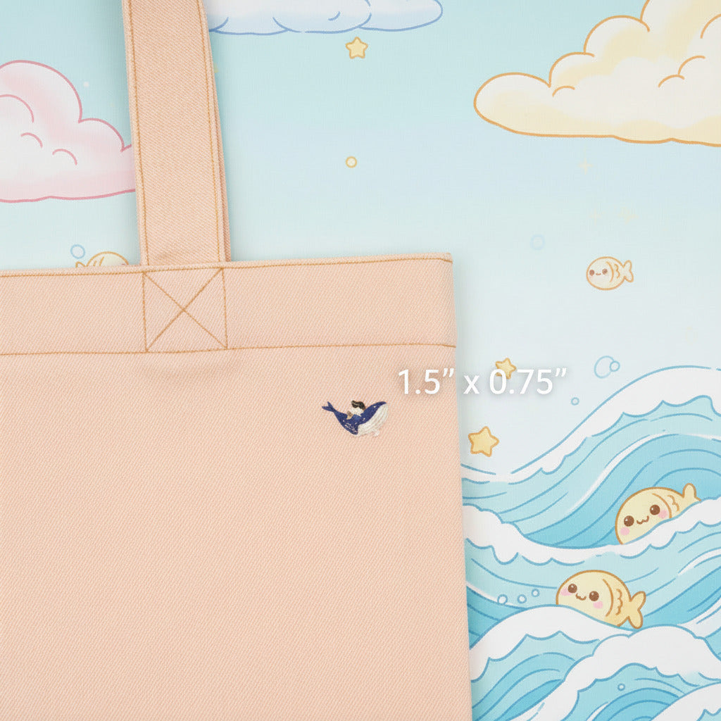 Close-up of a light blue denim tote bag with a small embroidered bird detail on the front, set against a plain light gray background.