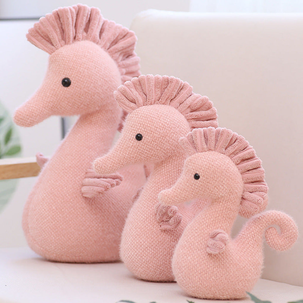 Three pink seahorse plush toys of different sizes on a light background