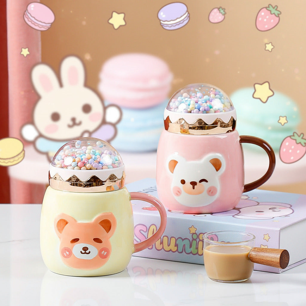 Two cute ceramic mugs with bear faces and dome lids filled with colorful beads, styled on a white surface with a book and a small glass of coffee in front. The mug on the left is pale yellow with a pink handle and a peach bear face.
