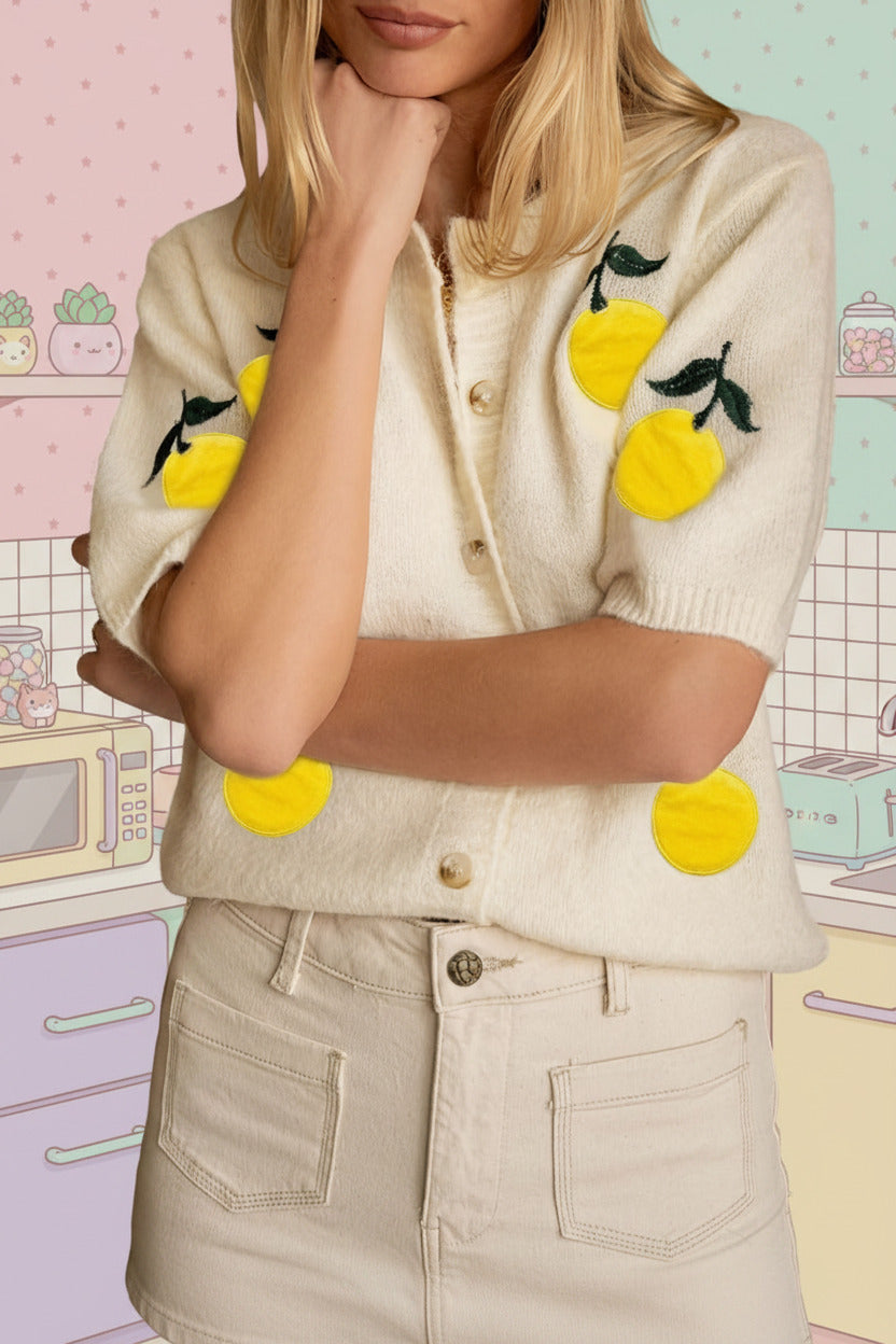 Person wearing a cream-colored cardigan with lemon designs in a kitchen setting