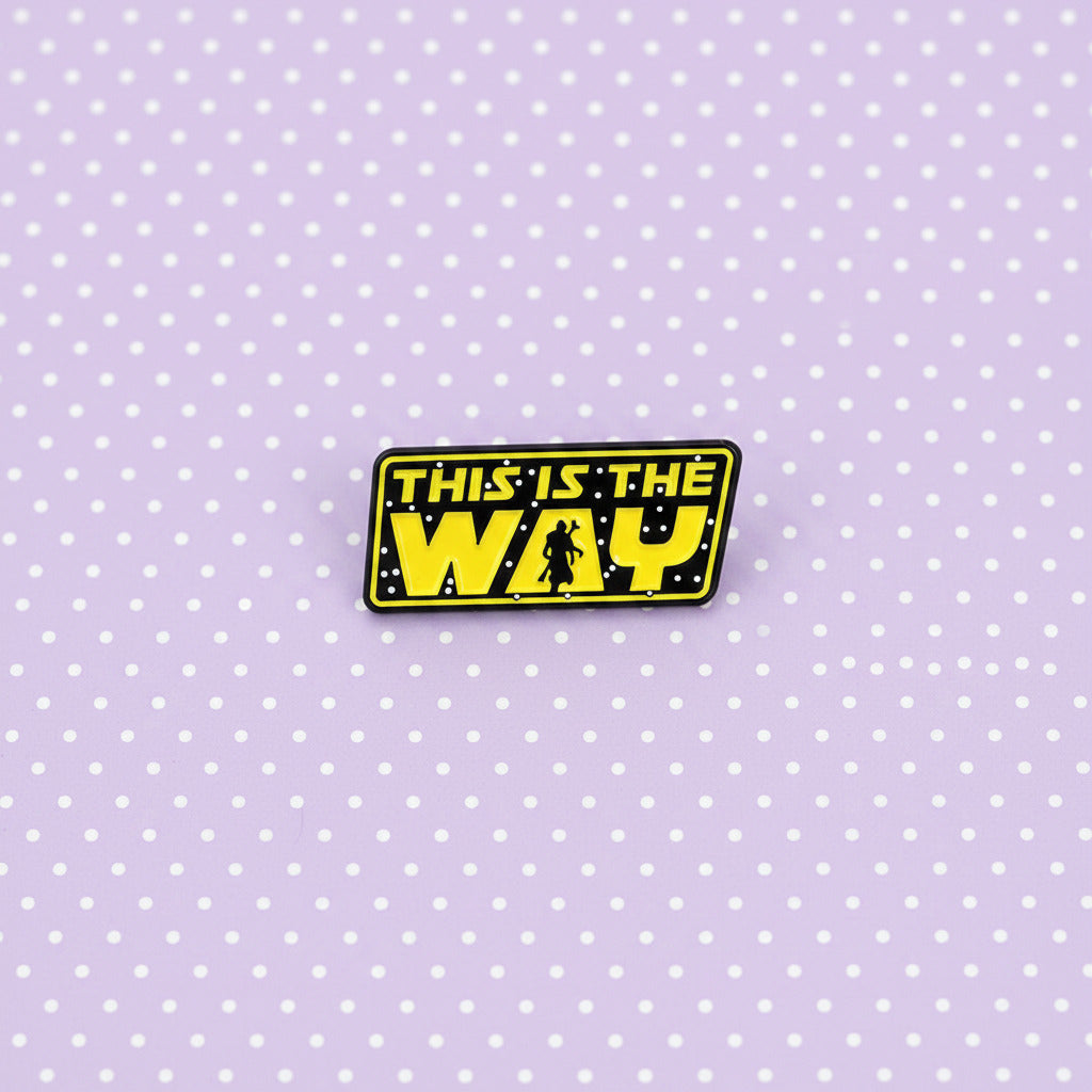 A rectangular enamel pin featuring the iconic yellow and black Star Wars logo text that reads 'THIS IS THE WAY' with a small silhouette of a stormtrooper, shown on a light lavender background.