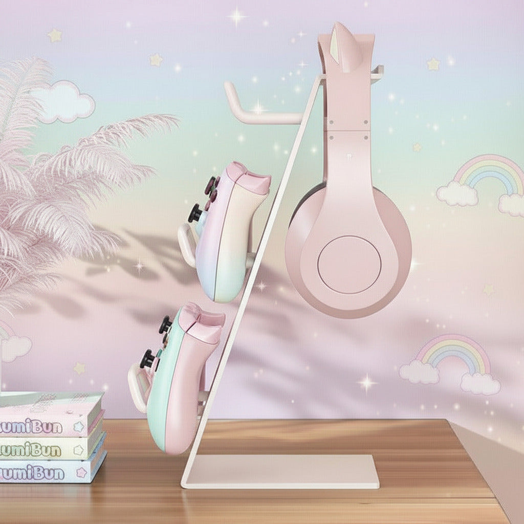 A pastel pink headphone displayed on a white wall-mounted stand, with two matching pastel headphones hanging on the side. The setup is placed on a wooden surface against a dreamy pastel wall with clouds, stars, and rainbows.