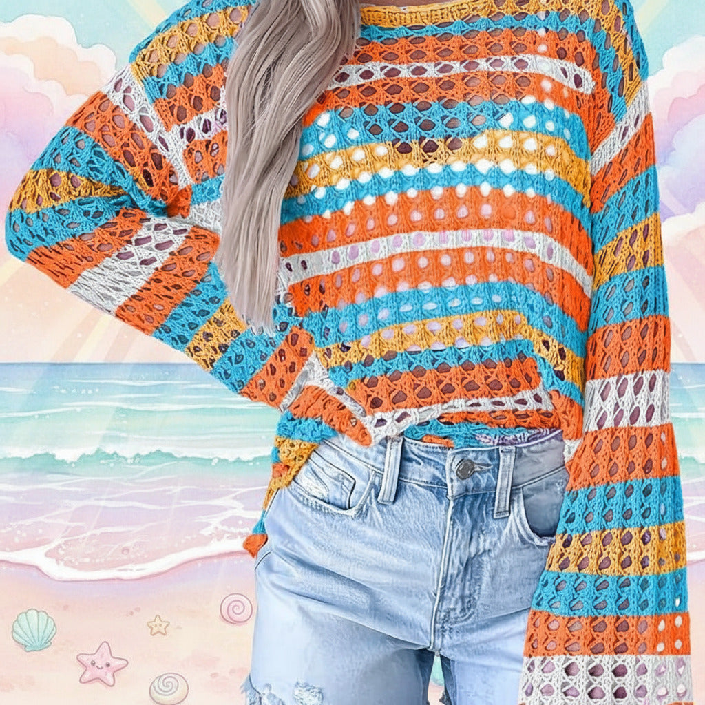 A person wearing a colorful striped crochet knit sweater with wide sleeves and light-wash denim jeans, standing against a light paneled wall.