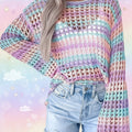 A person wearing a pastel striped open-knit crochet sweater with light blue jeans, shown from the shoulders to the hips against a light indoor wall.