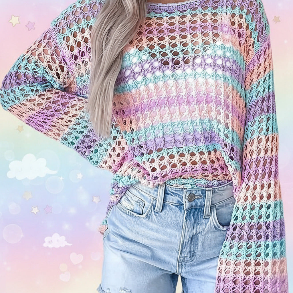 A person wearing a pastel striped open-knit crochet sweater with light blue jeans, shown from the shoulders to the hips against a light indoor wall.
