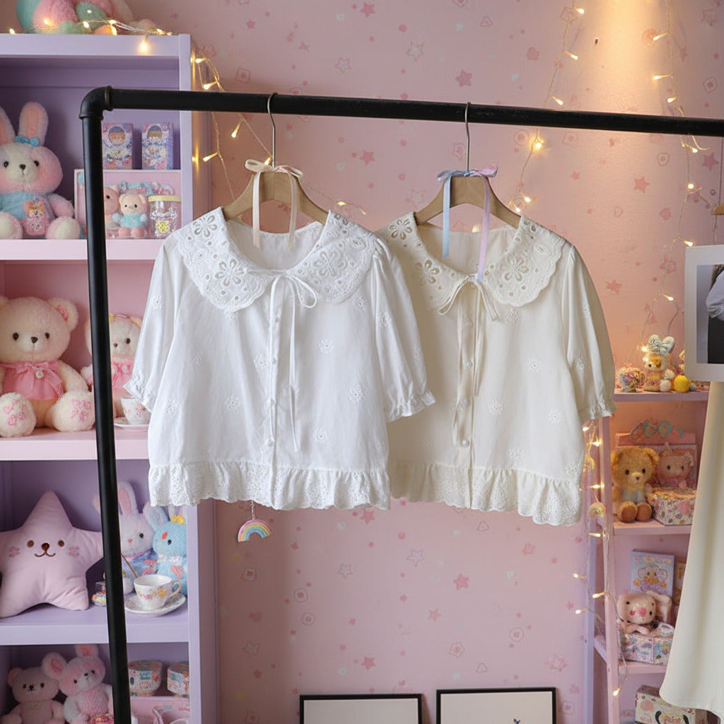 Two white blouses with lace collars hanging on a rack against a pastel rainbow colored neutral wall.